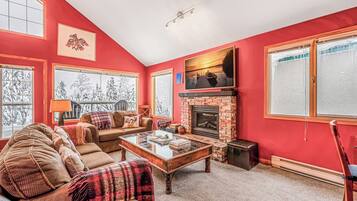 Cozy living room with a fireplace, leather sofa, and large windows offering views of the outdoors.