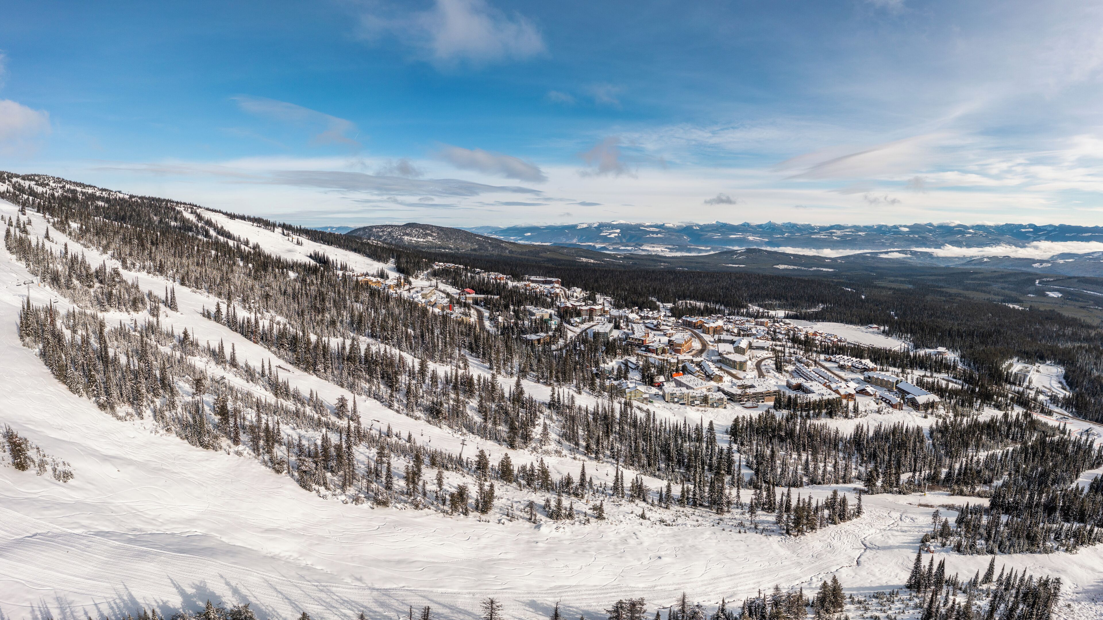 A snow-covered mountain town with buildings clustered together, surrounded by dense forests and snow-covered slopes.
