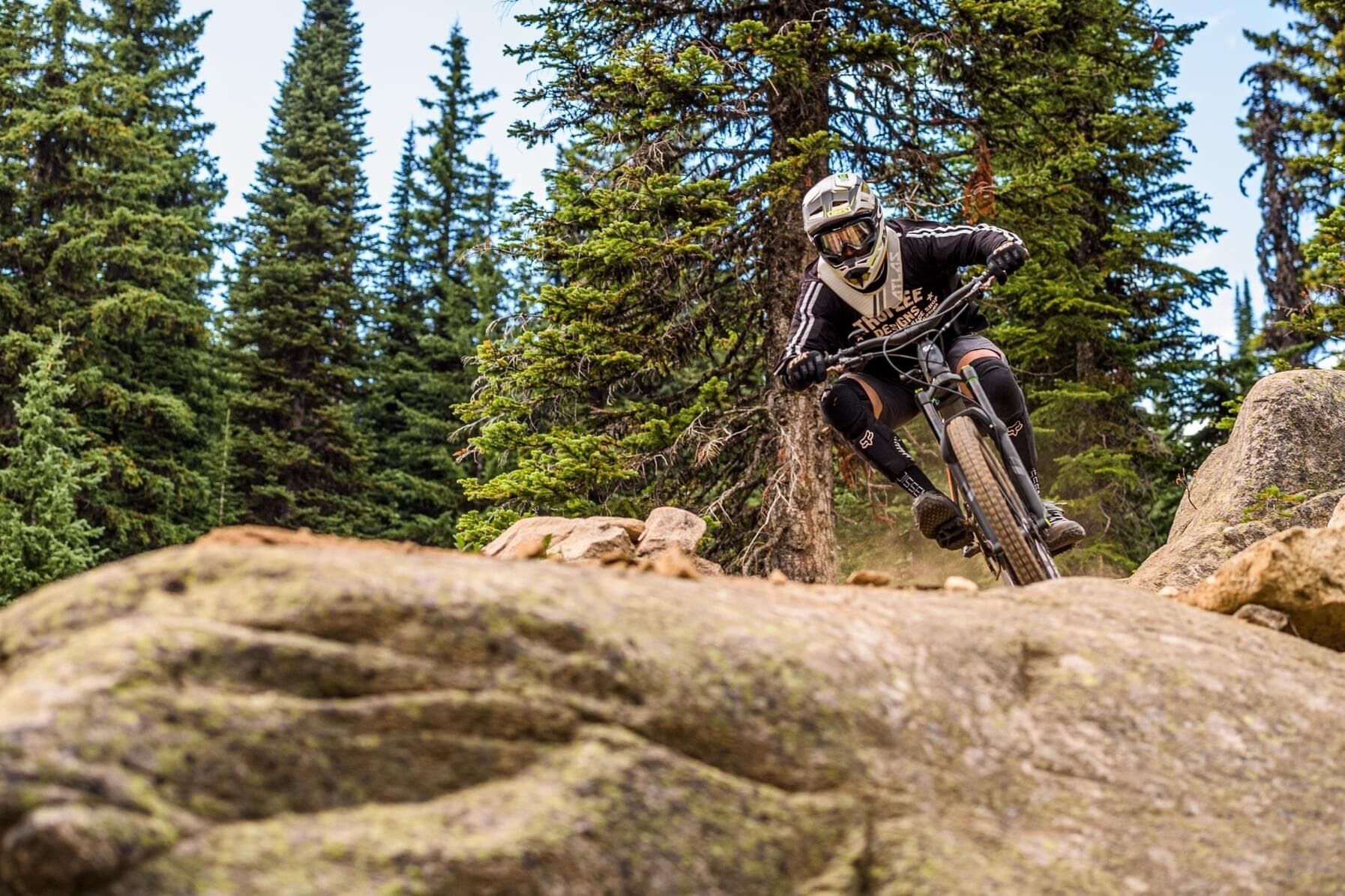Ein Mountainbiker auf felsigem Gelände, im Hintergrund Bäume.