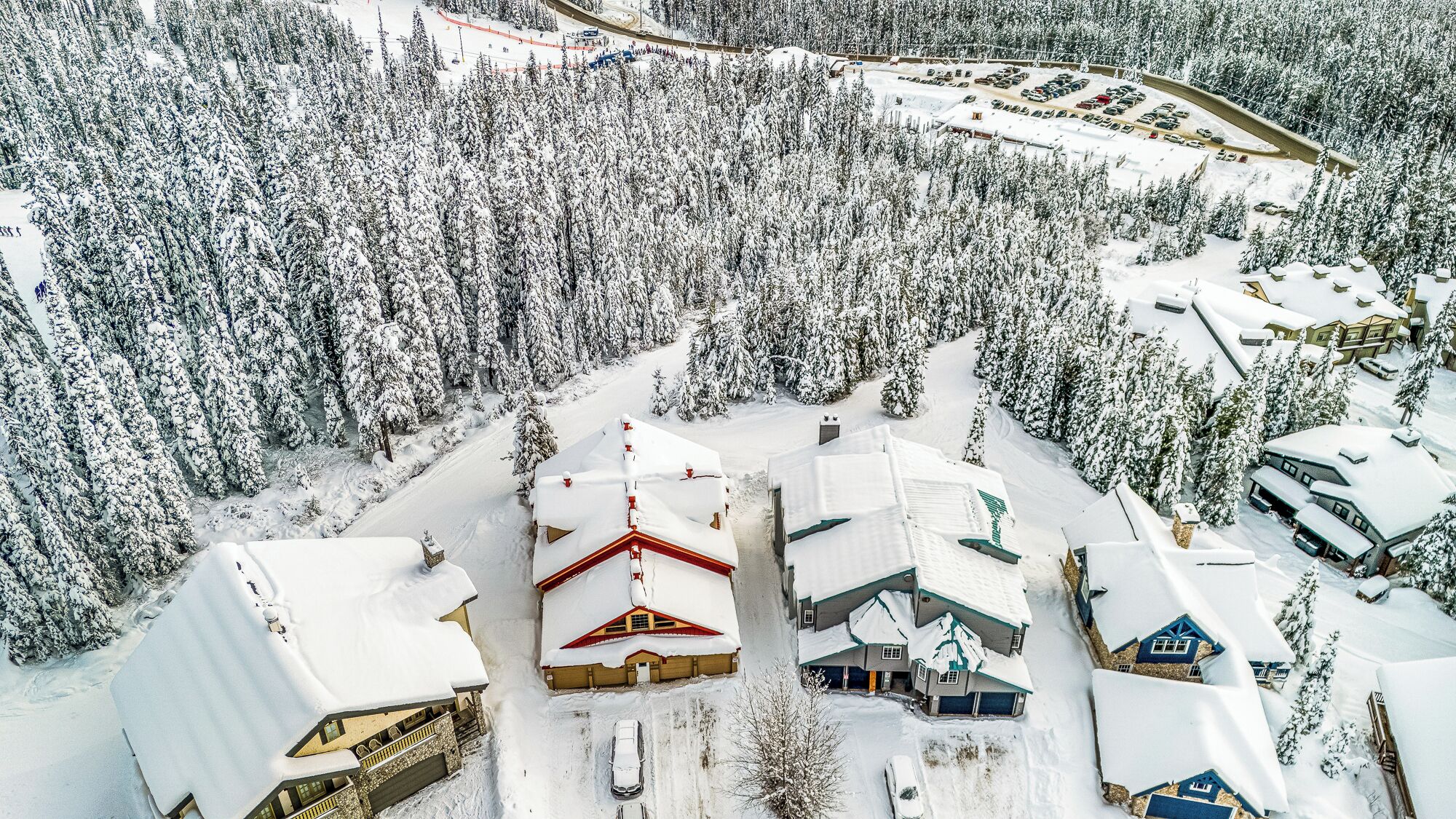 A snow-covered resort with multiple buildings, including a large lodge with a red roof and several smaller cabins.