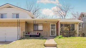 Ein zweistöckiges Haus mit Garage, einer Veranda mit Bank und einem kleinen Garten.