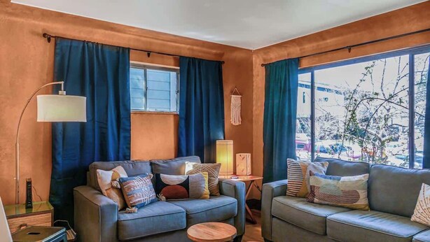 Ein modernes Wohnzimmer mit zwei grauen Sofas, runden Holztischen und einer Stehlampe.