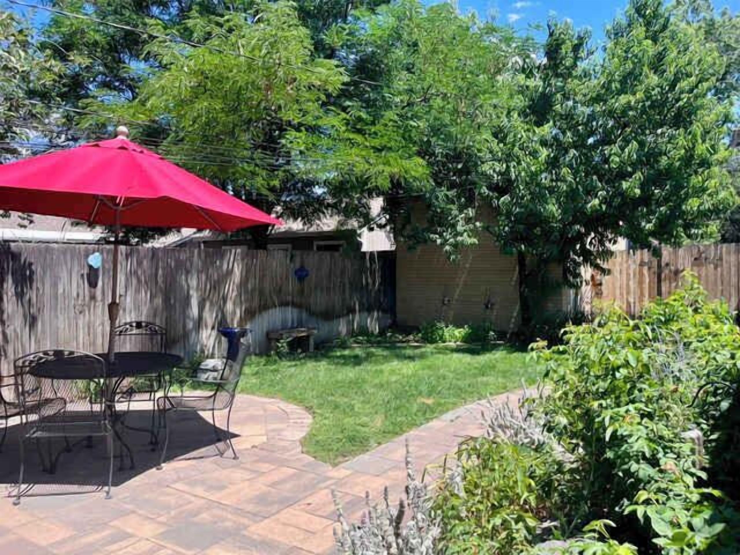 A backyard with a patio, a red umbrella, and a wooden fence.