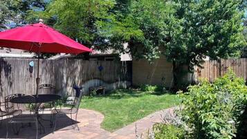 A backyard with a patio, a red umbrella, and a wooden fence.