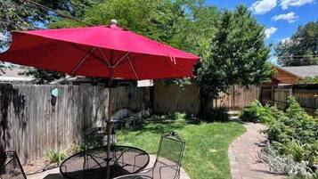 Une terrasse extérieure avec un parasol rouge, des chaises en métal et un chemin piétonnier à motifs en chevrons.