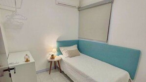 A small, neatly arranged bedroom with a single bed, a bedside table with a lamp, a small cabinet, and an air conditioning unit on the wall. - Cozy House in Curitiba (São Lourenço Curitiba)