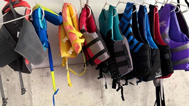 A rack of various life jackets hanging on a wooden shelf.