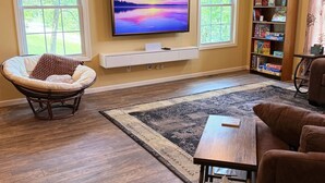 Un soggiorno con televisione a schermo piatto, una poltrona in vimini, un tavolino da caffè e una libreria.