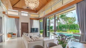 Una sala de estar moderna con un televisor grande, asientos cómodos y vista a una piscina.