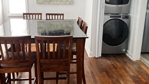 En matplats med ett träbord och stolar, en tavla som föreställer en gammal bil och ett tvättrum med tvättmaskin och torktumlare.