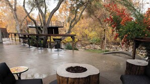 An outdoor patio area with a fire pit, seating, and a treehouse structure. - River Magic -Riverfront Luxury (Three Rivers)