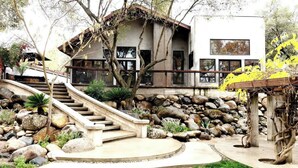 A modern house with a stone retaining wall, a wooden staircase, and a garden with rocks and plants. - River Magic -Riverfront Luxury (Three Rivers)