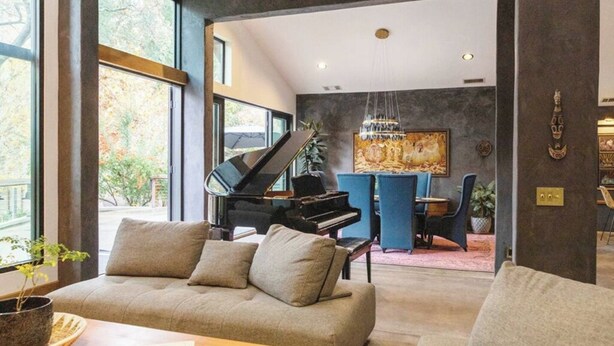 A modern living room with a piano, a sofa, and a dining area with a blue chair. - River Magic -Riverfront Luxury (Three Rivers)