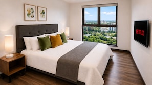 Une chambre d’hôtel avec un grand lit, une télévision, une fenêtre donnant sur la ville et des œuvres d’art accrochées au mur.
