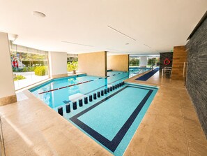 An indoor swimming pool with clear lanes, a lifebuoy, and a view of greenery outside.
