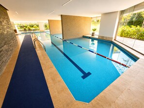 Une piscine intérieure avec des couloirs bien délimités, un sol bleu et une vue sur la verdure environnante.
