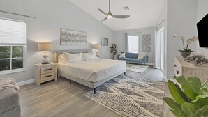 A modern bedroom with a large bed, bedside tables, a ceiling fan, and a view of the outdoors.
