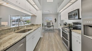 A modern kitchen with white cabinets, a granite countertop, stainless steel appliances, and a view of the outdoors.