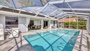 An outdoor swimming pool with a glass enclosure, surrounded by lounge chairs and a covered patio area.