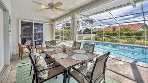 A covered patio with a pool, dining table with placemats, chairs, and a ceiling fan.