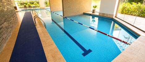 An indoor swimming pool with clear lanes, a blue floor, and a view of greenery outside.