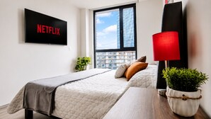 A hotel room with a bed, a TV displaying 'NETFLIX,' a window with a city view, a red lamp, and a plant on the nightstand. - Stylish High-Rise Escape: Pool, Hot Tub & Cinema, King-Size Bed and High-Speed WiFi. (Ciudad de México)