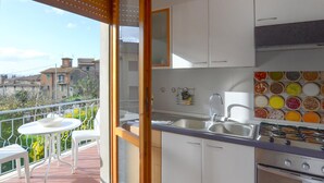 Un balcón con mesa y sillas blancas, una cocina con gabinetes blancos, un lavamanos y una estufa.