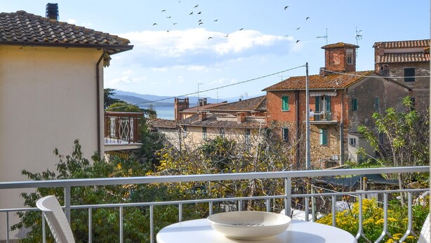 Un balcón con mesa y sillas, con vistas a un pueblo costero de edificios tradicionales y al mar.
