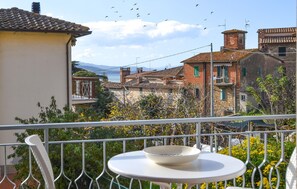 Un balcon avec une table et des chaises, donnant sur une ville côtière aux bâtiments traditionnels et offrant une vue sur la mer.