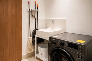Une buanderie équipée d’un lave-linge, d’un évier et d’outils de nettoyage.