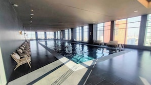 A large indoor swimming pool with clear water, surrounded by lounge chairs and large windows.
