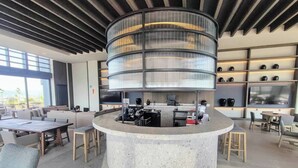 A modern bar area with a circular counter, bar stools, and a seating area with sofas and tables.