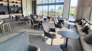 A modern indoor seating area with round tables and chairs, a sofa, and a TV on the wall.