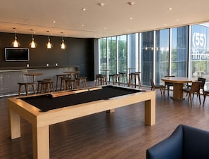 A modern indoor pool table with surrounding seating, large windows, and a visible number (55) on the glass.