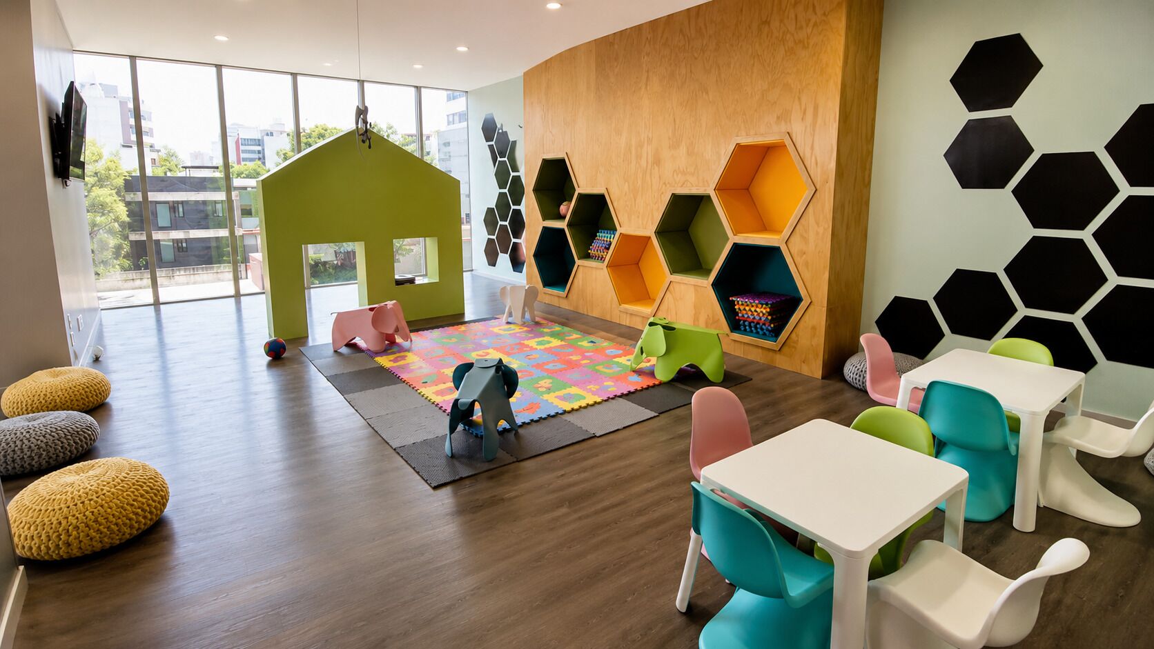A children's play area with a green playhouse, hexagonal storage units, and colorful seating.
