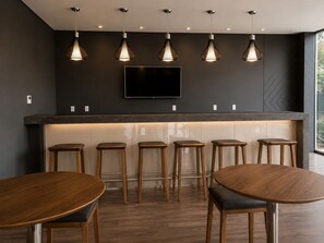 A modern bar area with a flat-screen TV, pendant lights, and wooden stools.