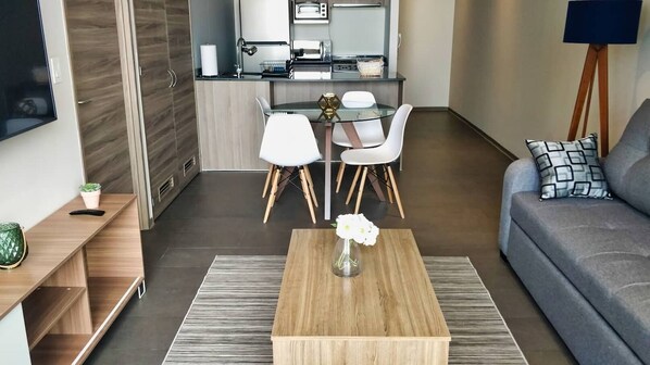 Un salon moderne avec une table basse en bois, un canapé et un coin repas avec des chaises blanches.