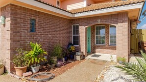 Una casa residencial con fachada de ladrillo, una puerta principal y un pequeño porche con macetas.