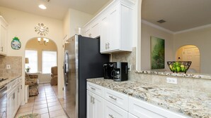 Una cocina con armarios blancos, un refrigerador negro, encimera de granito y una cafetera.
