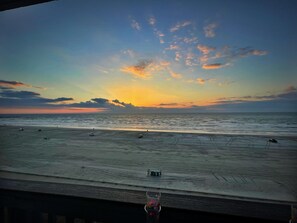 A beach view with a sunset, vehicles on the sand, and a clear sky.