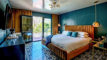 A modern hotel room with a large bed, a TV, a dining area, and a balcony with a view.