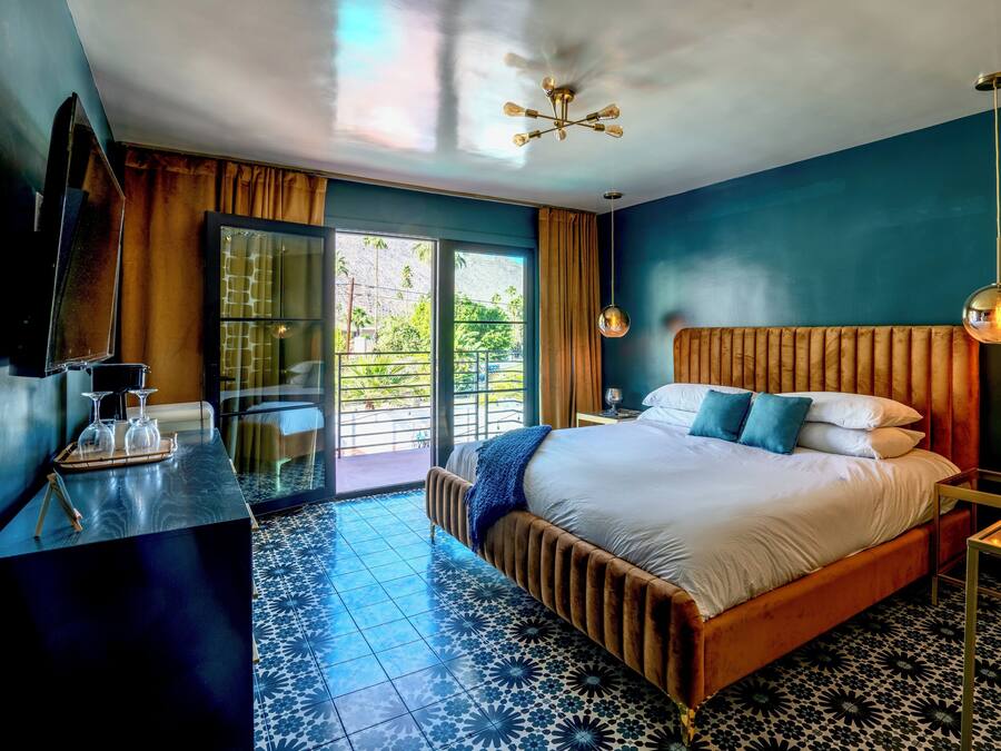 A modern hotel room with a large bed, a TV, a dining area, and a balcony with a view.