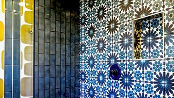 A bathroom with a shower, a wooden bench, and a tiled wall with a geometric pattern.