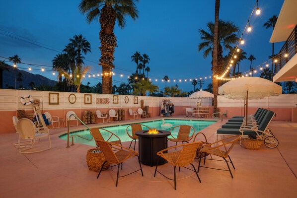 A pool area with lounge chairs, a fire pit, and string lights. - The Stardust Hotel (Palm Springs)