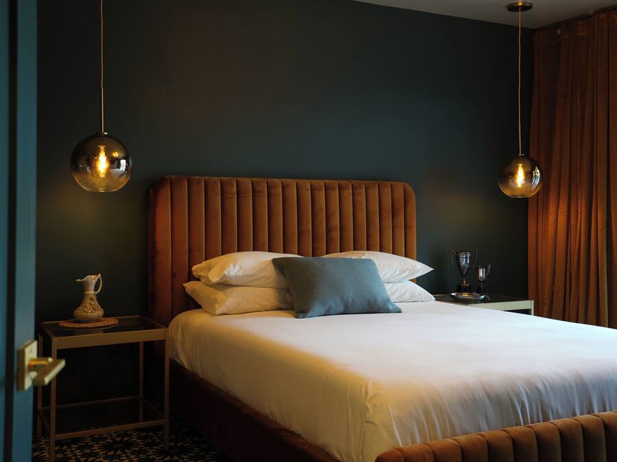 A neatly made bed with a wooden headboard, a bedside table with a lamp, and a vase on the nightstand.