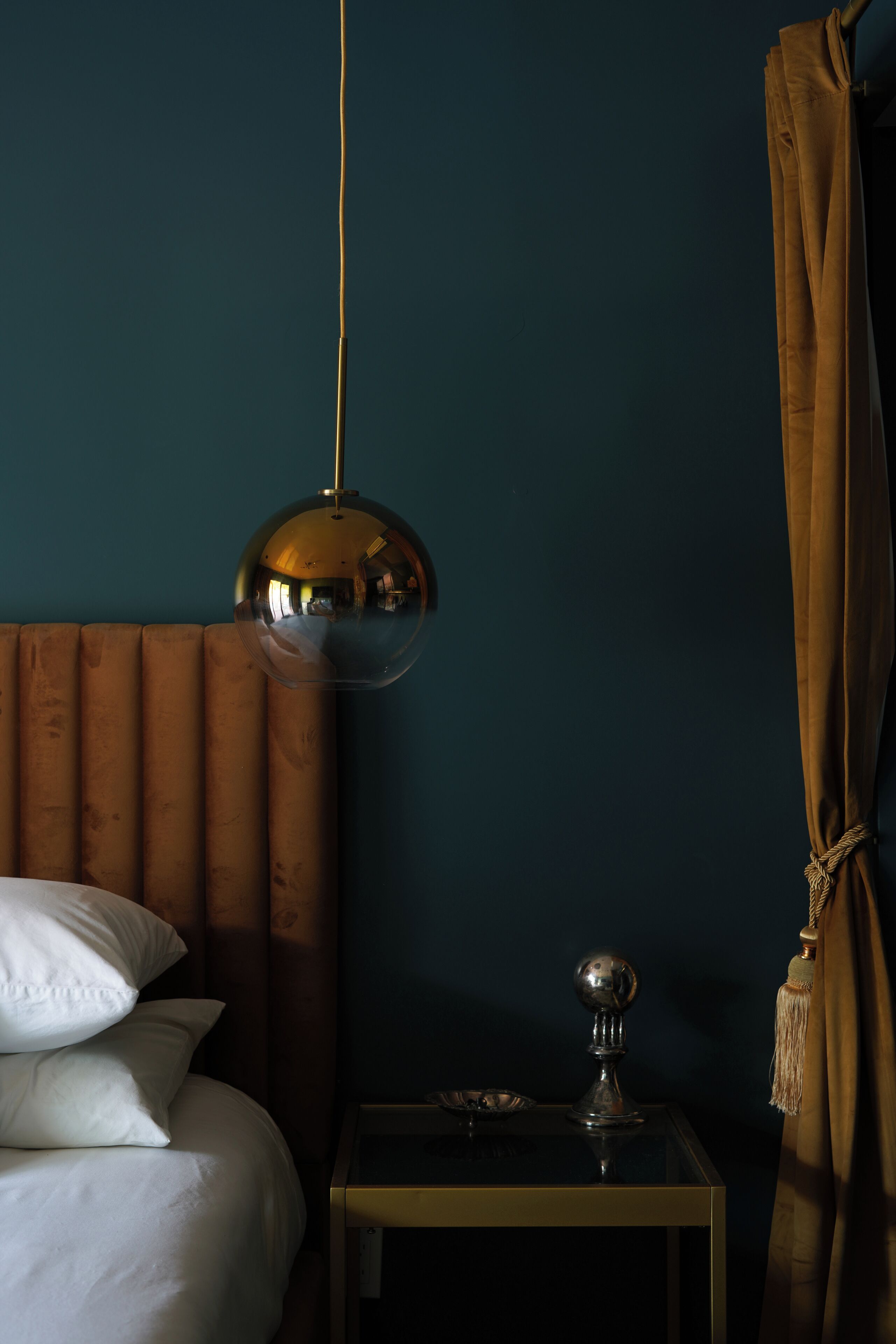Et værelse med en seng, et natbord, en hængende lampe og et gardin.
