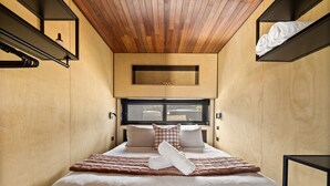 Ein modernes Schlafzimmer mit Holzboden, einem großen Bett mit weißer und brauner Bettwäsche und einem Fenster, das natürliches Licht hereinlässt.