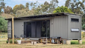 Eine kleine, eingeschossige Metallstruktur mit einer großen Schiebetür aus Glas, einer kleinen Veranda und einer Grillmöglichkeit.