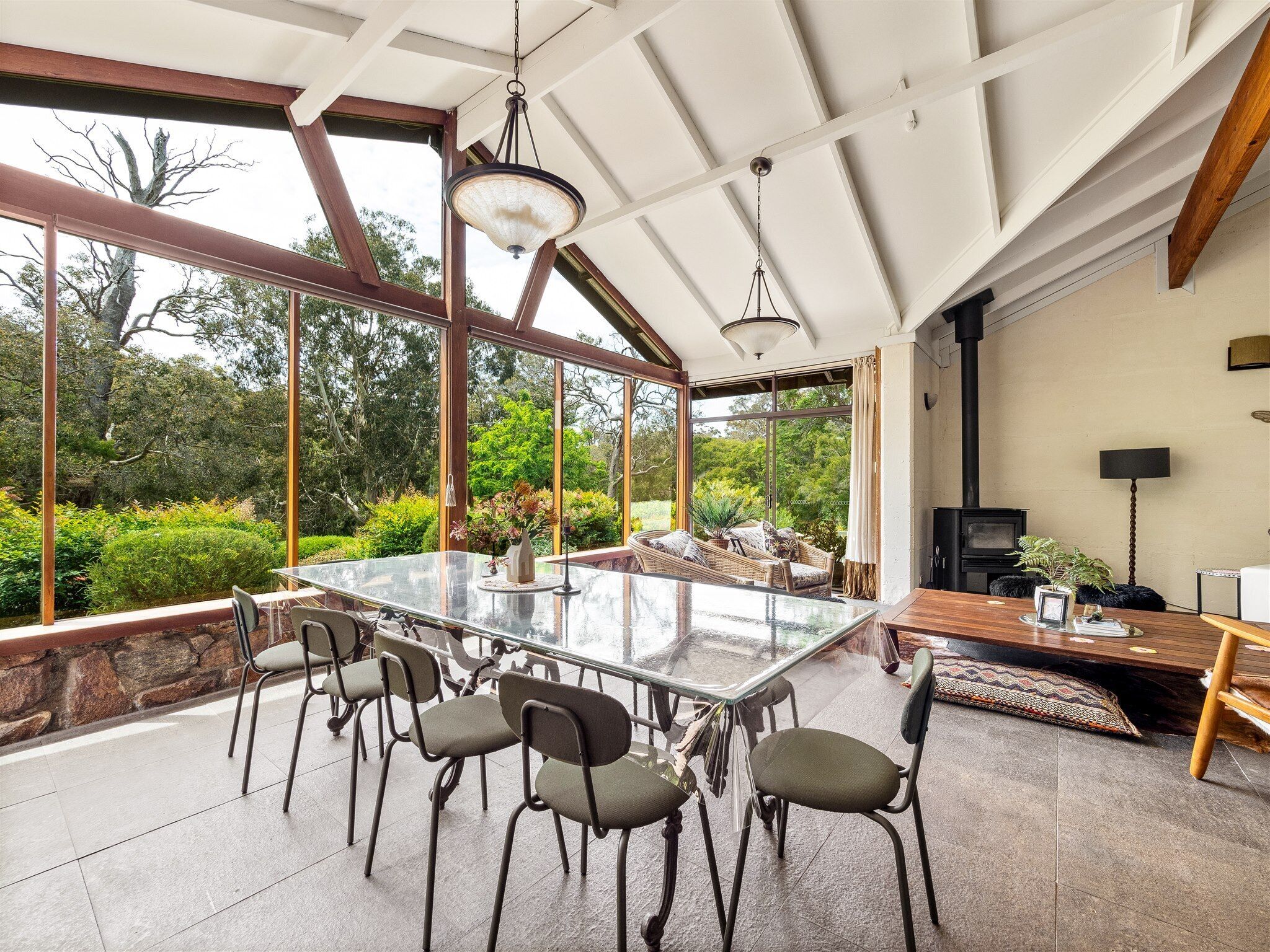 A spacious dining area with a large glass table, multiple chairs, and a view of the surrounding garden.
