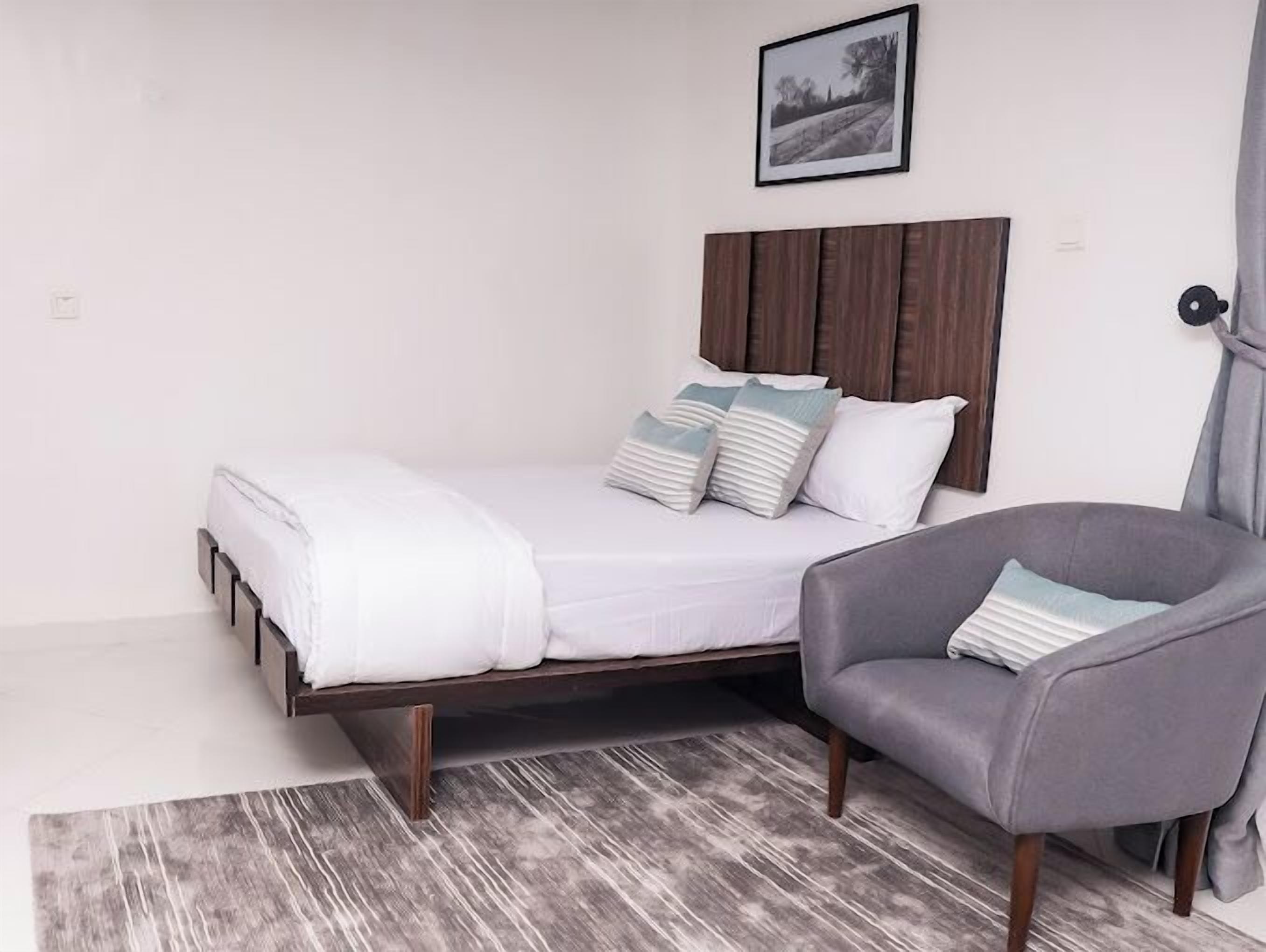A single bed with a wooden headboard, a grey armchair, and a grey rug.